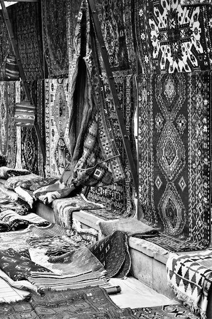 A detailed black-and-white photograph of a market stall on Chatsworth Road, showcasing a large, patterned rug hanging prominently on the exterior wall, with visible intricate geometric and floral desi